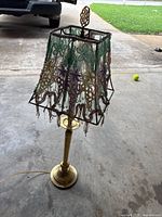Full view of antique brass table lamp with beaded floral lampshade, placed on concrete floor outdoors.