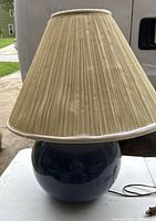 Side profile of lamp showing blue ceramic base and beige pleated lampshade with some discoloration