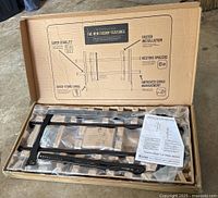 Open box showing black metal frame parts with packaging and installation instructions on top inside the box.