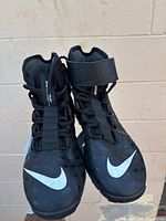 Front view of black Nike football cleats showing the white swoosh on toe area and lace-up front with ankle straps.