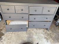 Grey wooden dresser with multiple drawers; some drawers are open and misaligned due to missing screws and repairs.