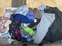 Top view photo showing variety of women's clothing items including pants, tops, hoodies, jackets, and accessories laid out on ground.