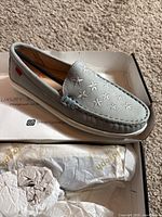 Photo of a light grey kids loafer featuring star embroidery on the top and moccasin-style stitching, displayed in an open box.