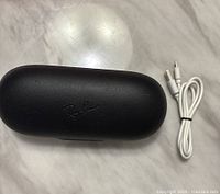 Closed black Ray-Ban hard charging case with USB charging cable beside it