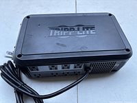 Front perspective of the black Tripp Lite power surge protector showing the power outlets and attached cable.