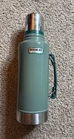 Vintage Stanley 2 Quart Classic Vacuum Bottle shown upright on carpet floor, displaying stopper and cup lid.