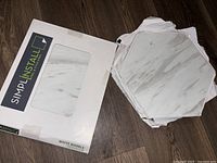 Three boxes of white marble hexagonal peel and stick vinyl tiles, one opened box showing tiles.