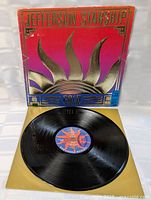 Vinyl record displayed partially outside the colourful front jacket showing label and gloss