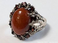 Front view of sterling silver ring showing large reddish-brown cabochon and garnet halo