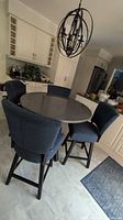Full view of round stone top table with four navy blue upholstered swivel chairs in kitchen