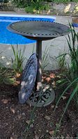 Greenish-brown resin bird bath next to a garden with plants and a pool in background