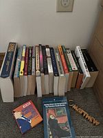 Full view of all books lined up against wall with two additional books out front and a wooden keychain beside them, on carpet