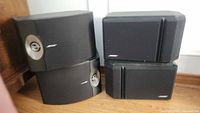 Two pairs of Bose stereo speakers placed together showing relative size and shape differences, black color with Bose logos visible.