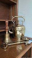 Full set of brass kettle, bell, large key, and spoon displayed on wooden shelf