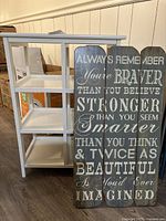White wooden cabinet with open shelves and glass side panels shown with motivational sign beside it.