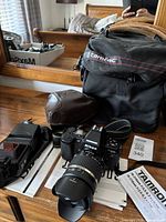 Overall arrangement: camera with lens mounted, flash, two carrying cases, strap and paperwork on dresser