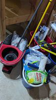 Photo of two mop buckets with red wringers, new mop heads inside buckets, mop handles standing upright, and cleaning gloves in one bucket.