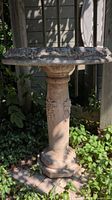 Full view of the concrete bird bath standing in garden area, showing round basin on pedestal with floral accents.