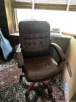 Front view of the rust-colored office chair showing tufted backrest, padded arms, and wood base with casters.
