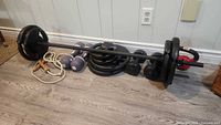 Barbell with black weight plates, two 5 lb purple dumbbells, additional weight plates, and a skipping rope with wood handles arranged on the floor