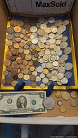 Full tray showing a variety of coins predominantly silver and copper tones arranged in rows with a US $2 bill in the foreground.