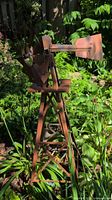 Side angle photo showing metal windmill in garden surrounded by plants with rust-like finish and four-legged metal tower.