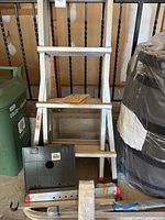 Front view of telescopic aluminum ladder with three visible steps, red safety tips, black plastic base piece next to ladder, and instruction manual on ladder steps.