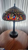 Full view of the table lamp showing domed stained glass look shade with floral patterns and black plastic base.