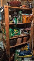 Wooden shelves with multiple gardening items including watering cans, bags of soil and fertilizer, pots, a lantern and other gardening supplies.