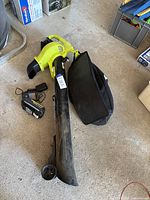 Ryobi leaf blower with collection bag, battery and charger laid out on a garage floor