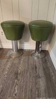 Pair of green vinyl vinyl cushioned swivel stools with round stainless steel bases, showing wear and need cleaning.