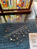 Two silver-tone bracelets, 16 assorted charms, and bee earrings laid out on a textured blue mat.