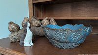Overall view of three items on a wooden shelf: pottery bowl, resin birds on branch, and Springer Spaniel figurine