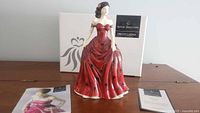 Porcelain figurine 'Jennifer' with box and two brochures seen behind the figure