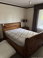 Full view of the oak-colored wood sleigh bed with mattress and box spring in bedroom setting