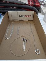 Wide view of all jewellery items including 5 necklaces and 1 pair of earrings placed in a cardboard tray, showing shapes and styles.