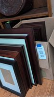 Stack of wood frames in various brown colors with white mats, leaning against a box