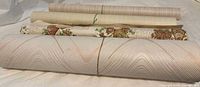 10 rolls of vintage wallpaper shown rolled and laid out together, featuring various colors and patterns including stripes, floral designs, and textured neutrals.