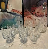 Photo of crystal cut and etched wine glass sets including decanters, glasses and a pitcher, displayed against an abstract painted background.