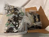 Large quantity of various cabinet and door hardware items inside plastic container and box including ceramic knobs, metal backplates, and handles.