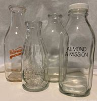 Four glass milk bottles grouped together showing variety in size, embossing, and labeling.