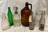 Full view of all 7 vintage bottles showing variety in color and shape including amber jug and green soda bottle
