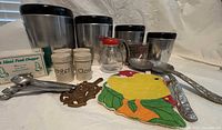 Photo showing the full lot with West Bend canisters, spice containers, kettlebell measuring spoons, chicken pot holder, trivet, and serving spoons.
