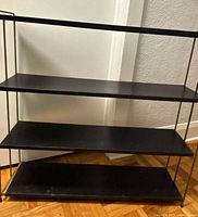 Front view showing four black shelves and bronze frame with visible wear on shelves.