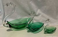 Three green and clear glass swan-shaped dishes displayed side by side showing sizes and form