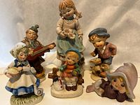 Six porcelain or ceramic figurines with children in various poses and outfits, showing all figurines for identification of set contents