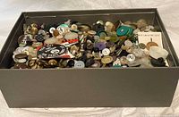 Top view showing a shoe box filled with many buttons of different colors, sizes, and materials including pearl and metal.