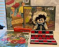 Cloth doll, checkers set with box, children's record covers visible, and packaged puzzles laid out on fabric background