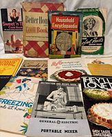 Photo showing all 12 vintage cookbooks and household booklets arranged on a white surface, titles and covers visible