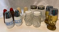 Six pairs of assorted vintage salt and pepper shakers on white surface, various glass styles and top caps